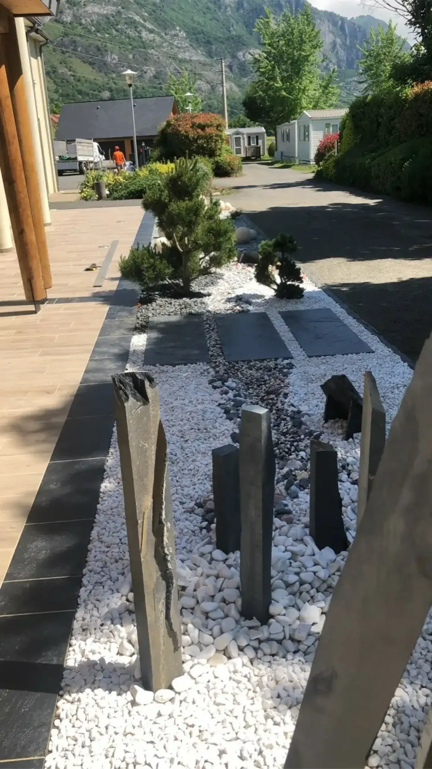 Jardin minéral avec graviers blancs, dalles d’ardoise et arbustes devant un paysage montagneux