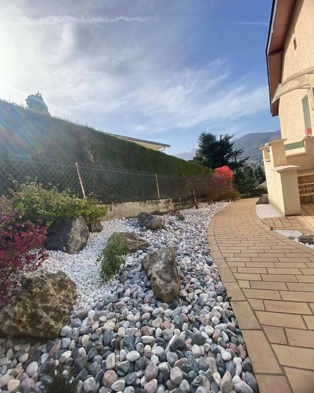 Jardin minéral avec galets, rochers et chemin pavé devant une maison
