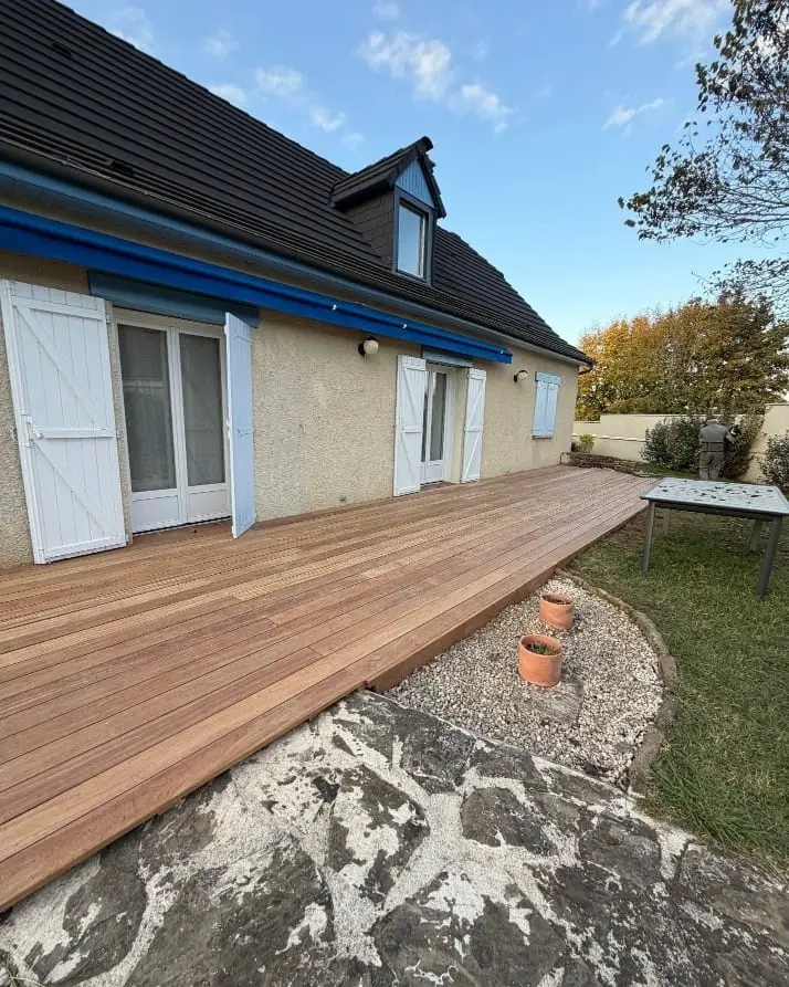 Terrasse en bois aménagée devant une maison avec une bordure de graviers