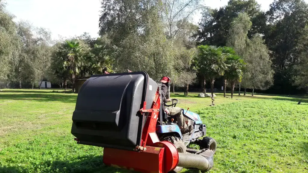 Paysagiste conduisant une tondeuse autoportée sur une grande pelouse arborée